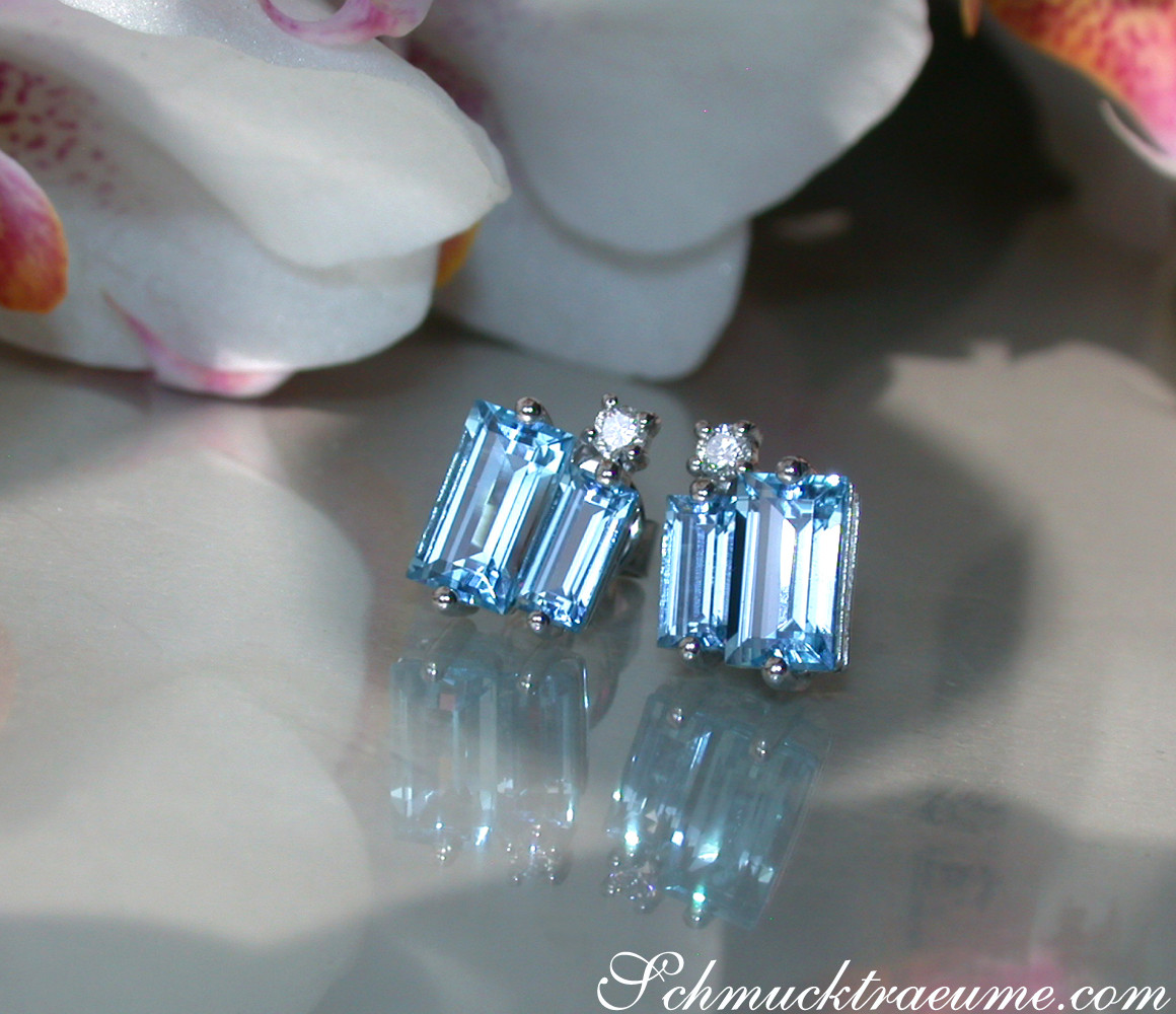 Blautopas Baguette Ohrstecker mit Diamanten, elegant auf glänzender Oberfläche, Blüten im Hintergrund.