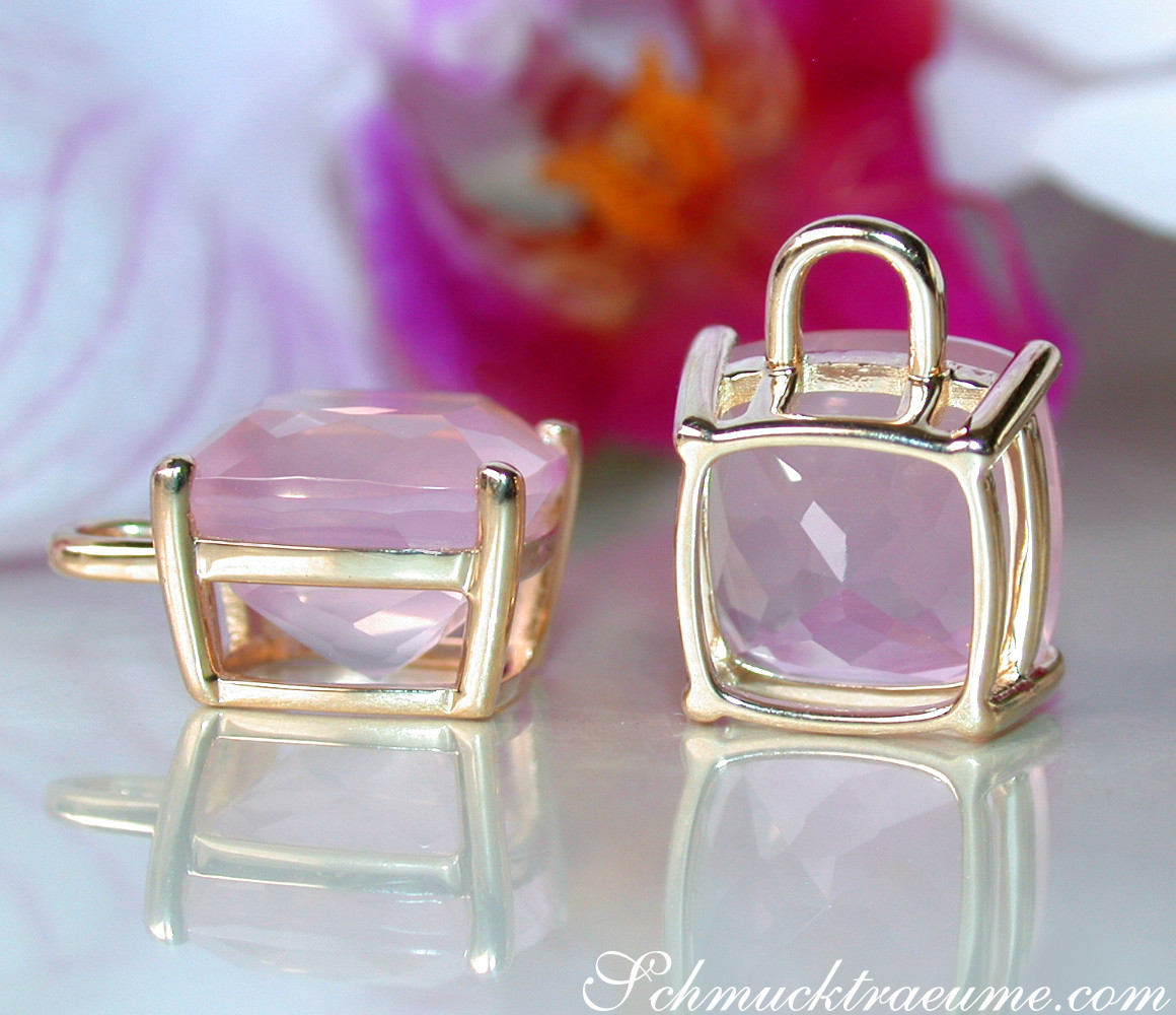 Goldene Kissenohrringe mit rosa Rosenquarzsteinen auf glänzender Oberfläche