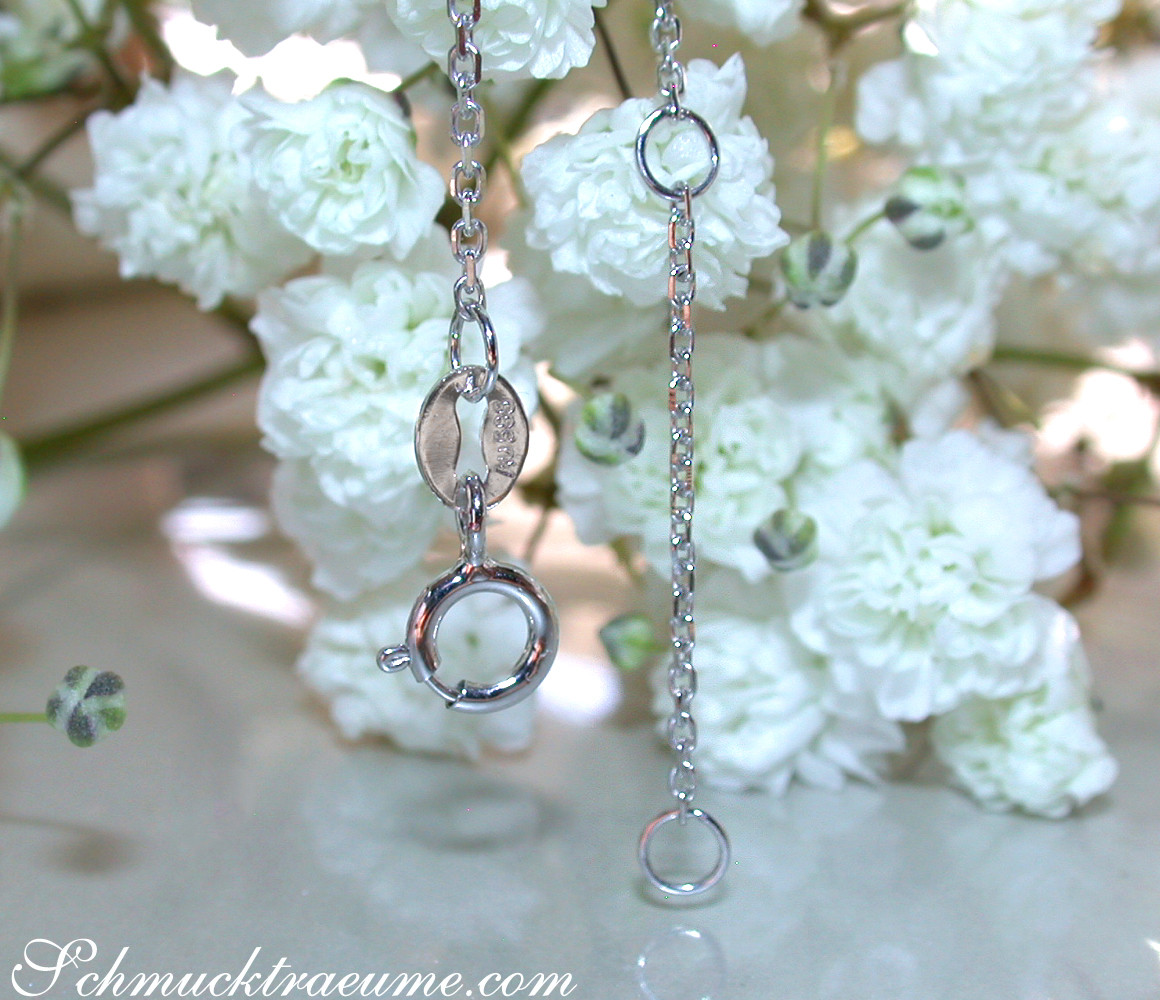 Silberkette mit Blautopas und Diamanten vor weißen Blüten, Detailaufnahme.