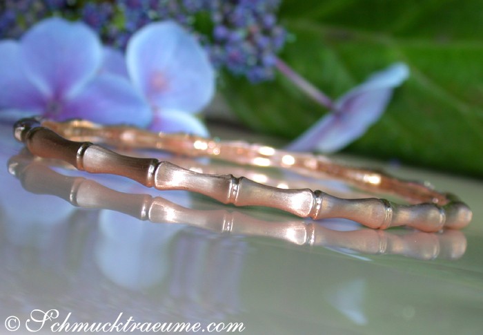 Roségold Armbänder im Bambus-Design auf Spiegeloberfläche, Hintergrund mit Blüten