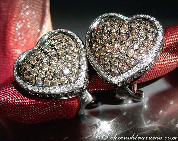 Herz-Ohrringe aus Weißgold 585, verziert mit braunen und weißen Brillanten, auf rotem Samt liegend.