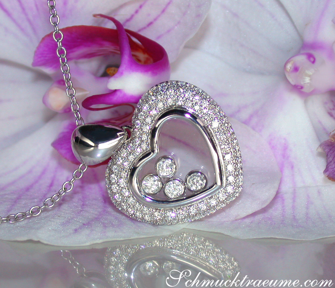 Herz-Anhänger mit Brillanten und Diamanten, zarte Kette, Orchideenblüte im Hintergrund