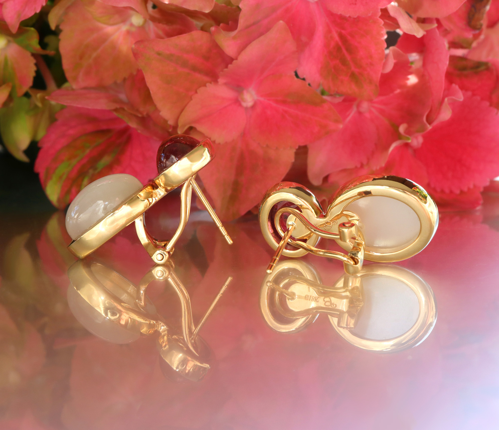 Goldene Ohrringe mit Rubellit und Mondstein, Detailaufnahme vor roten Blüten.