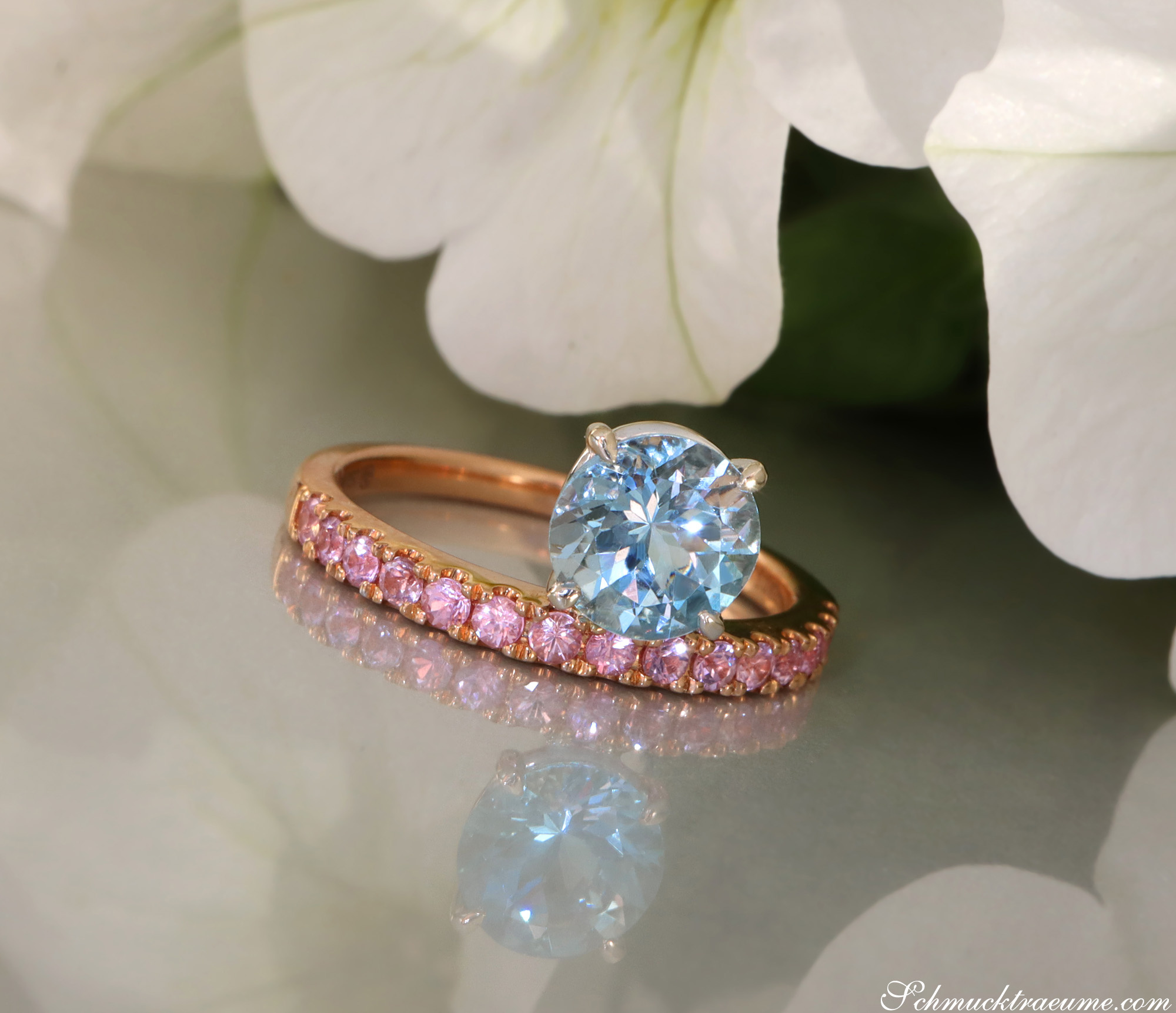 Raffinierter Aquamarin-Ring mit rosa Saphiren, detailreiches Design, goldene Details, blühende Blume im Hintergrund