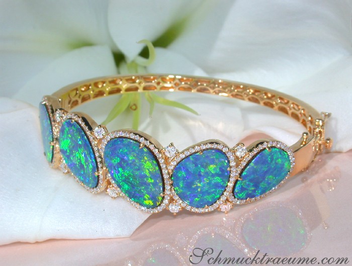 Gelbgold-Armreif mit Boulder Opalen und Brillanten auf weißem Blütenhintergrund
