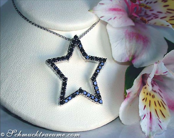 Schwarzer Diamantenstern-Anhänger auf Kette, Detailaufnahme, Blüten im Hintergrund.