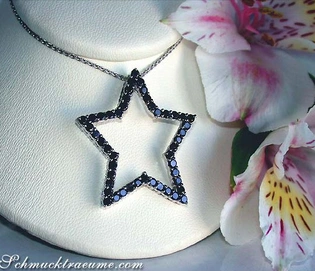 Schwarzer Diamantenstern-Anhänger auf Kette, Detailaufnahme, Blüten im Hintergrund.