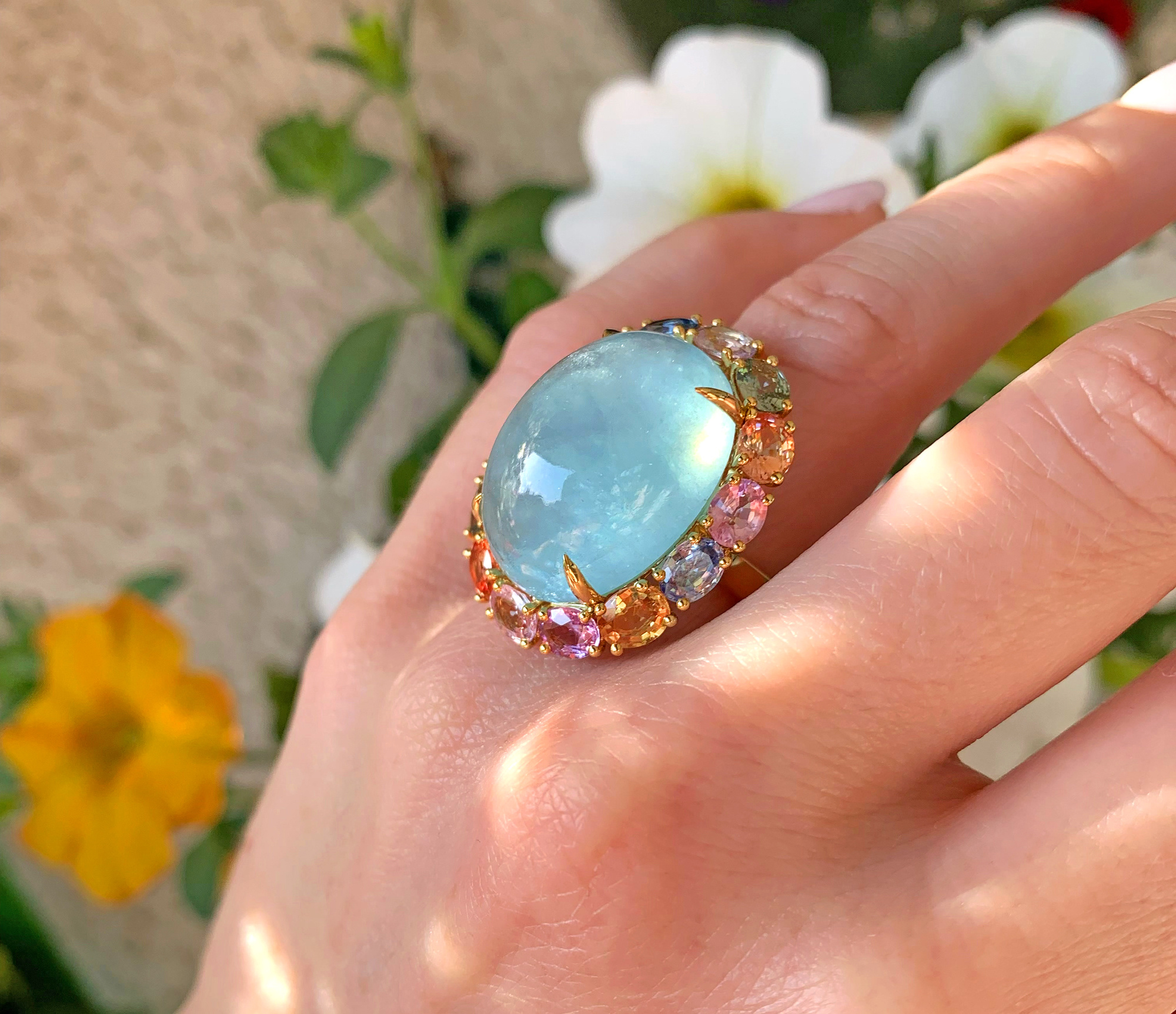 Opulenter Milky Aquamarin-Ring mit Multicolor Saphiren, Gelbgold 750, im Hintergrund Blüten