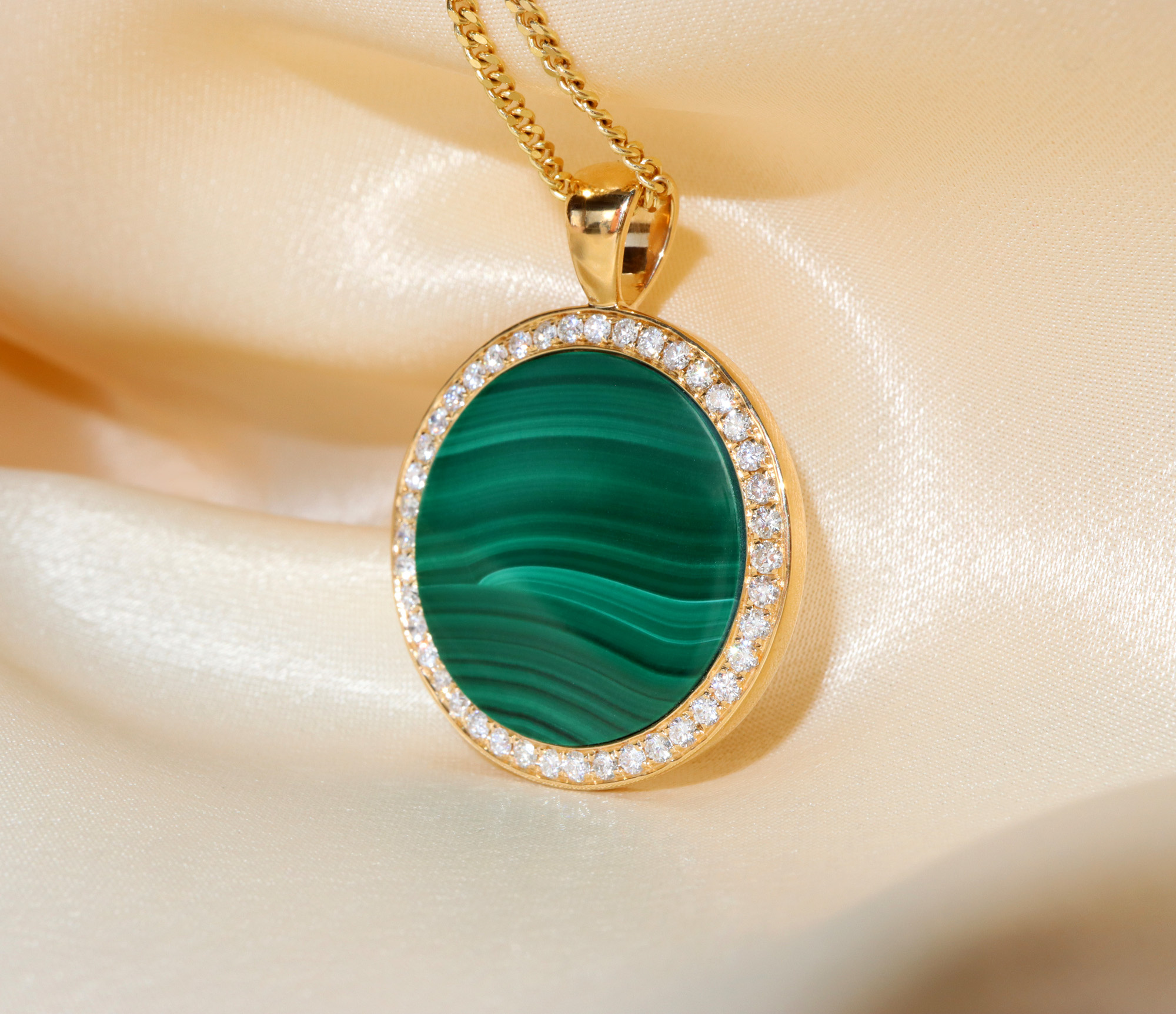 Goldener Malachit-Anhänger mit Brillanten, detailreich, auf cremefarbenem Stoff.