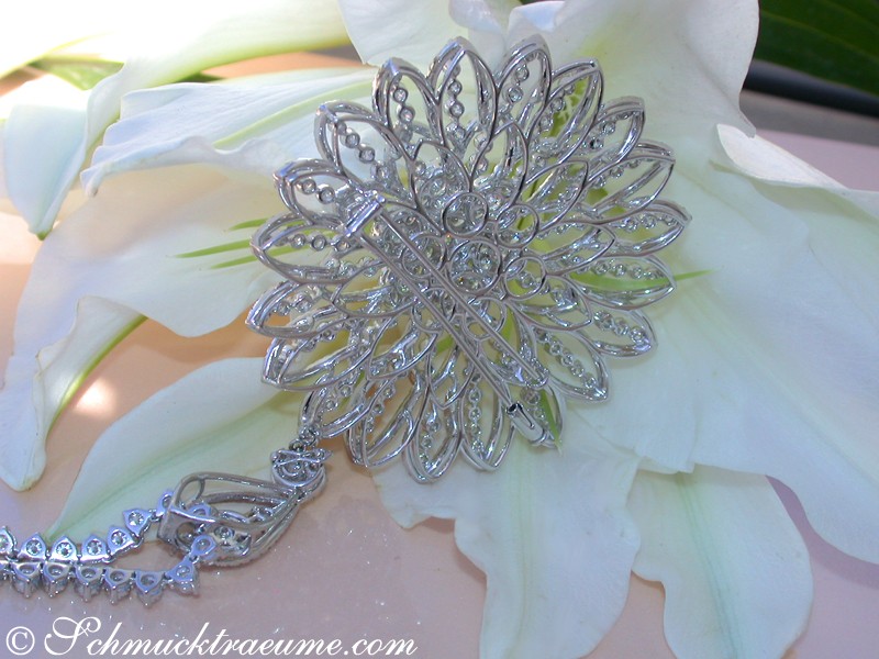 Blumendetail mit silberner Brosche, filigraner Blütenstruktur, weiße Lilien im Hintergrund.