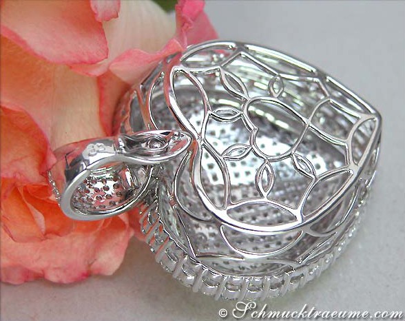 Silberner Herzanhänger mit feinem Muster, Detailaufnahme, rosafarbene Blume im Hintergrund