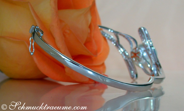 Silberner Armreif mit Südseeperle, Detailaufnahme, rosafarbene Blume im Hintergrund