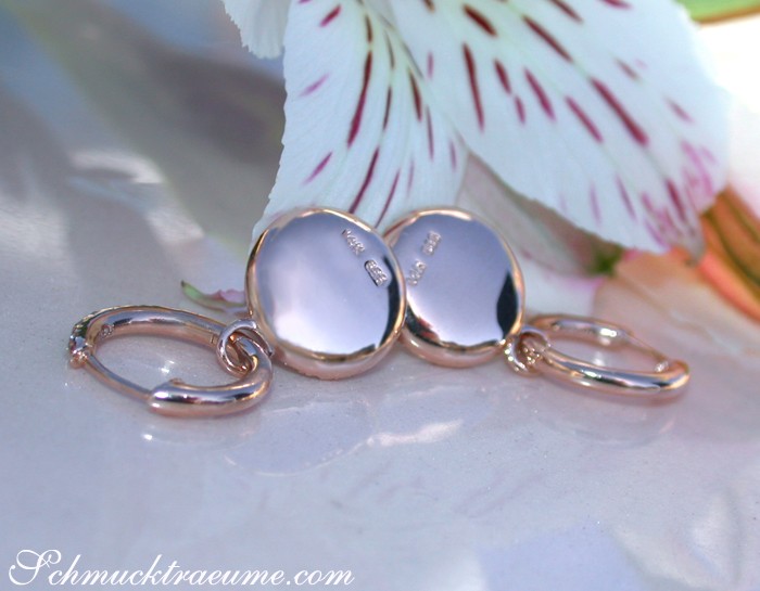 Roségold-Ohrringe mit Brillanten auf Blütenhintergrund