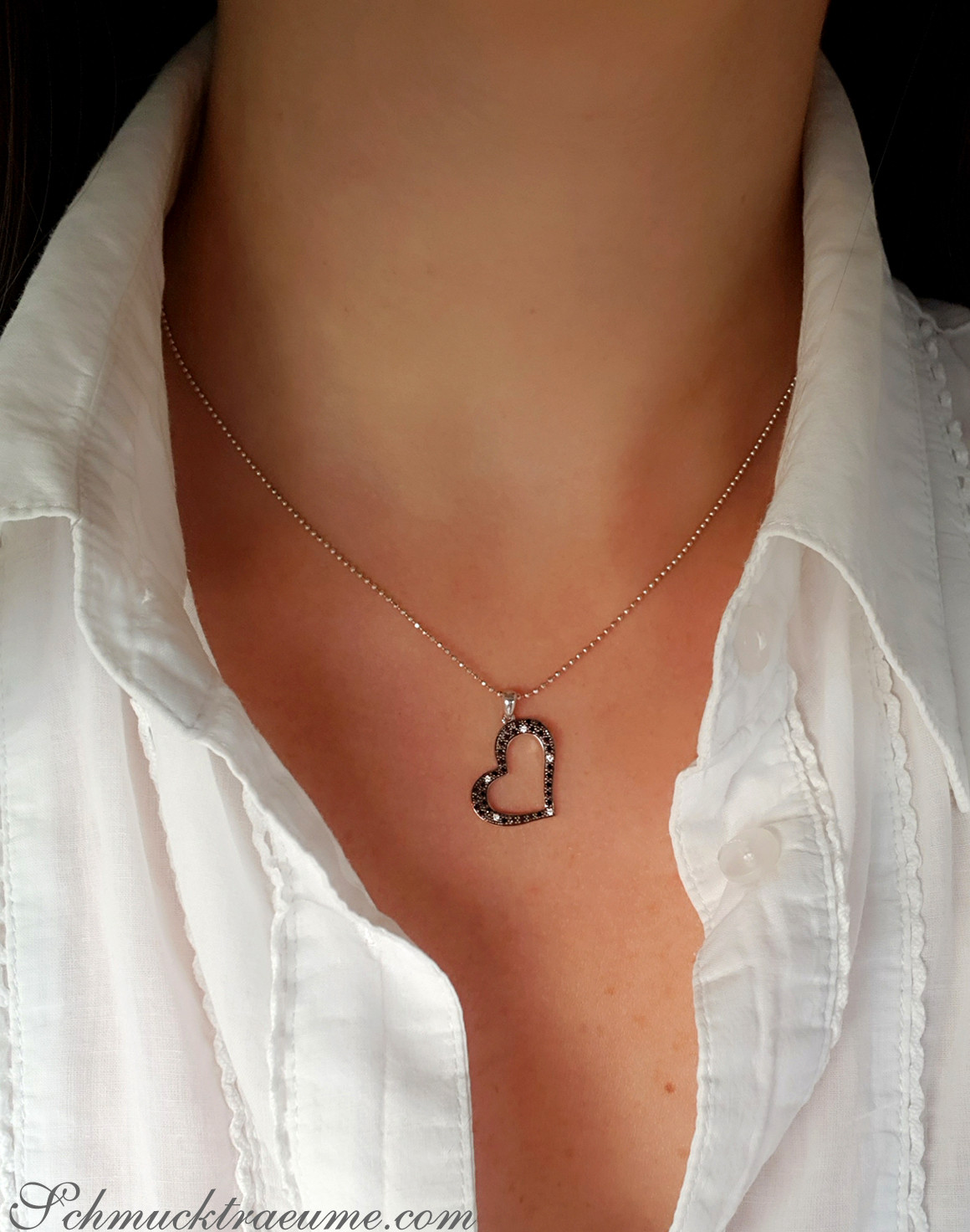Weißgold Herz-Anhänger mit schwarzen Diamanten, zarte Kette, trägt weiße Bluse.