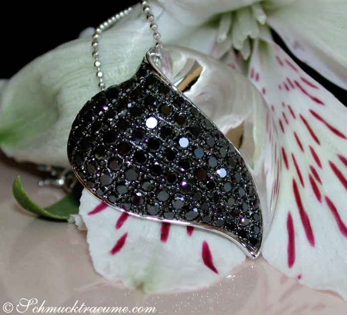 Schwarzer Diamant Herzanhänger mit Perlen, detailreiches Design, auf Blume liegend.