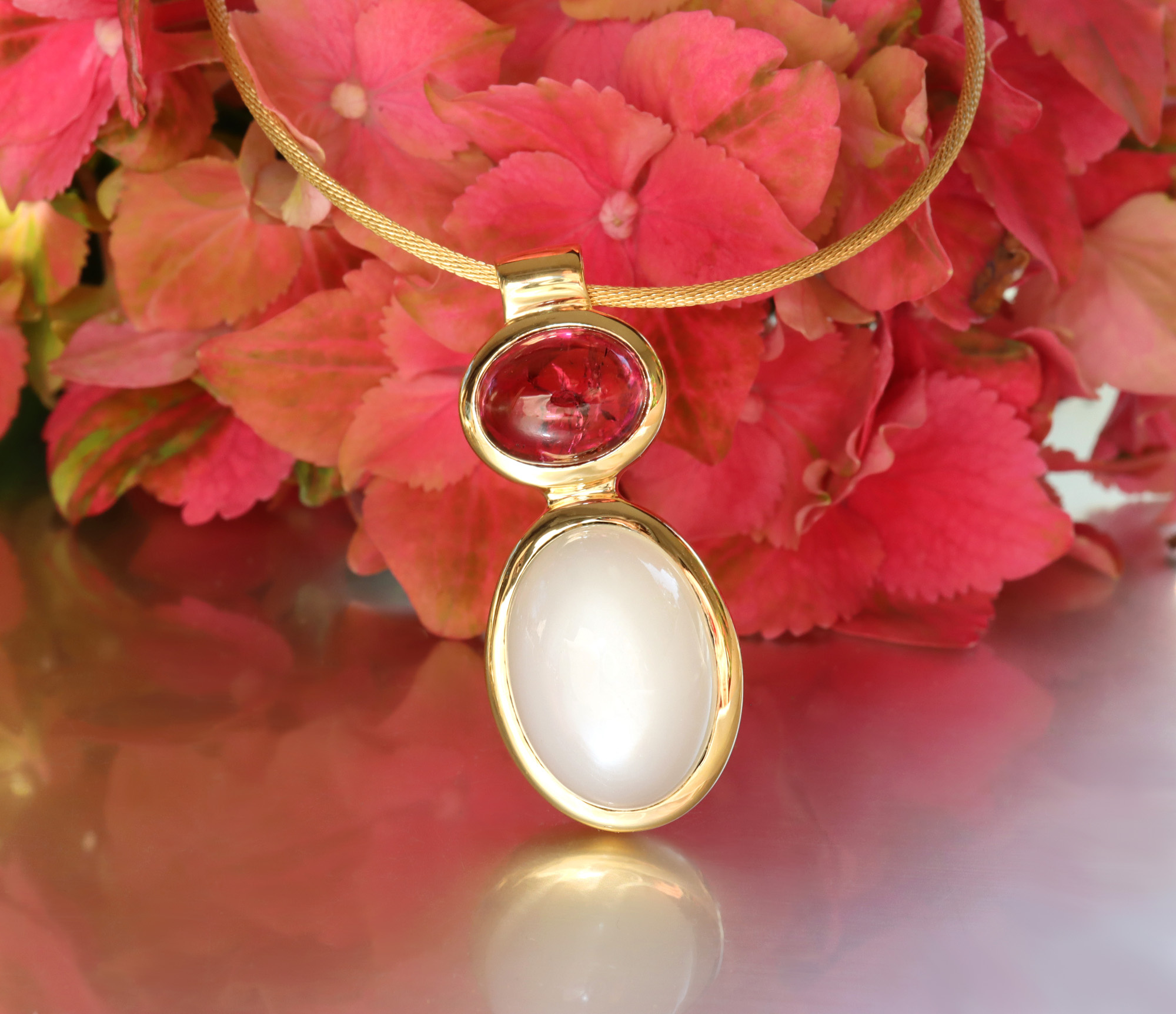 Goldene Halskette mit Rubellit und Mondstein, vor rosa Blüten.