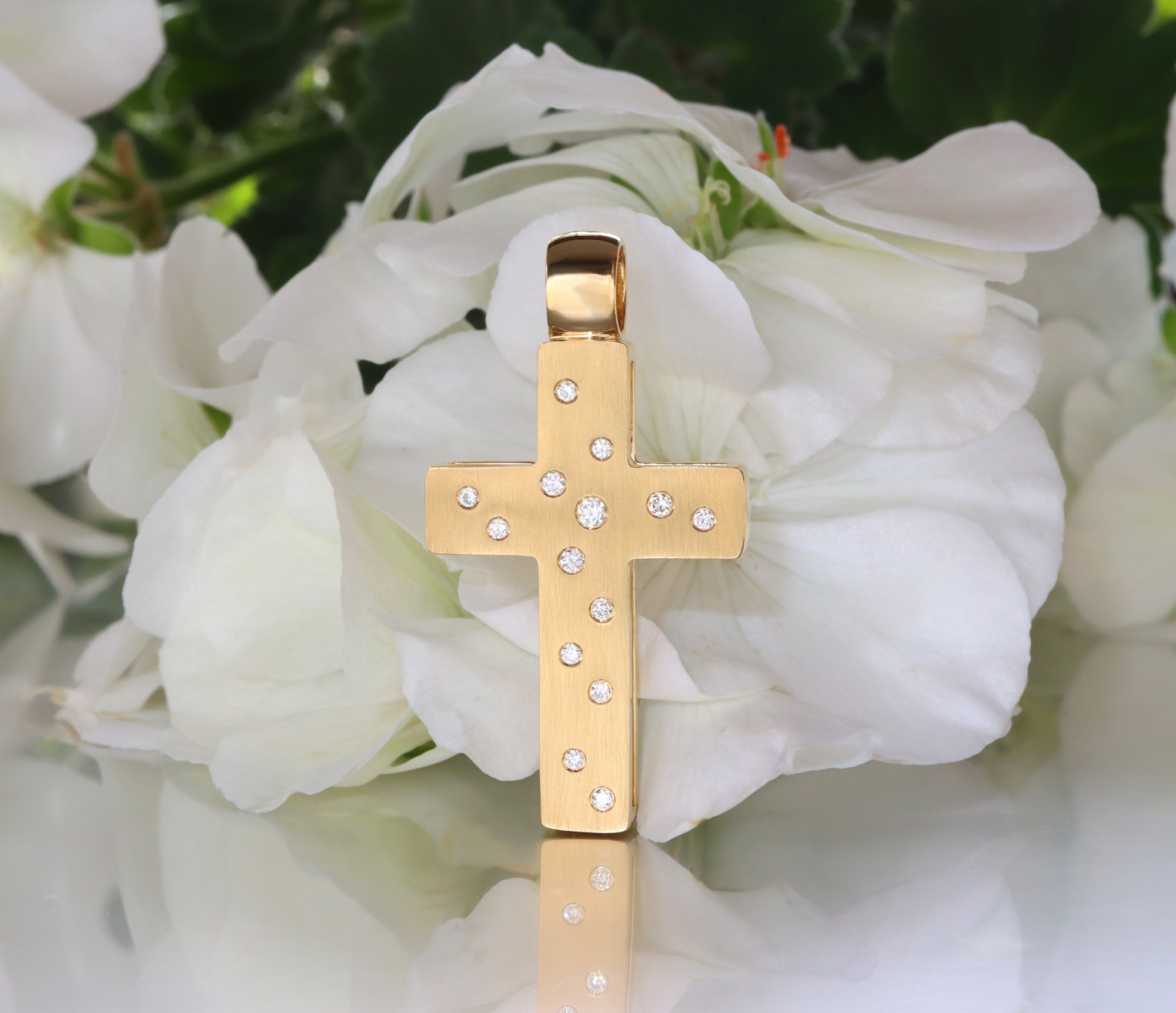Goldener Kreuzanhänger mit Brillanten, vor weißem Blütenhintergrund