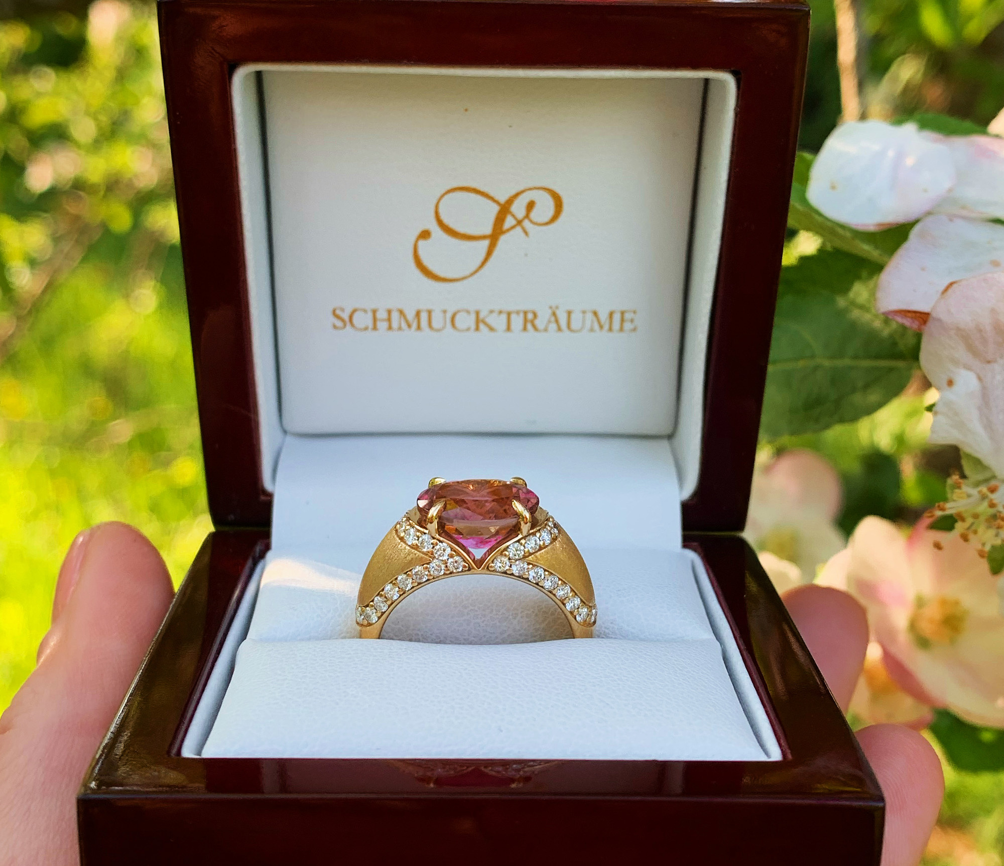 Goldener Turmalin-Ring mit Diamanten im Schmuckkasten vor Blüten.