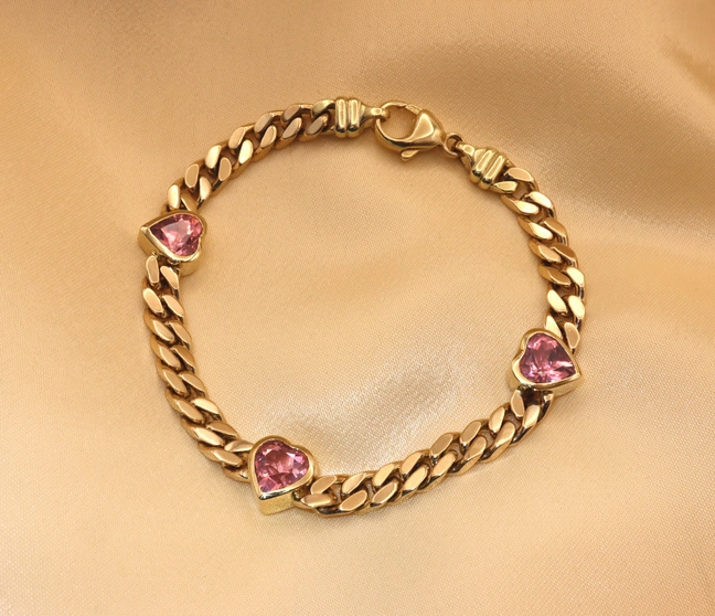 Goldene Panzerarmband mit rosa Turmalinherzen, detailreich, auf glänzendem Stoff liegend. Goldene Panzerarmband mit rosa Turmalinherzen, detailreich, auf glänzendem Stoff liegend.