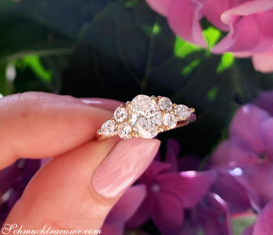 Femininer Diamant Solitär Ring im Ovalschliff, Brillanten und Marquise Diamanten, Gelbgold 750, vor lila Hortensienblüten.