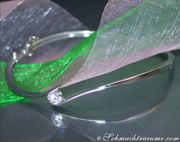 Silberner Armreif mit Brillant auf grünem Organza vor dunklem Hintergrund