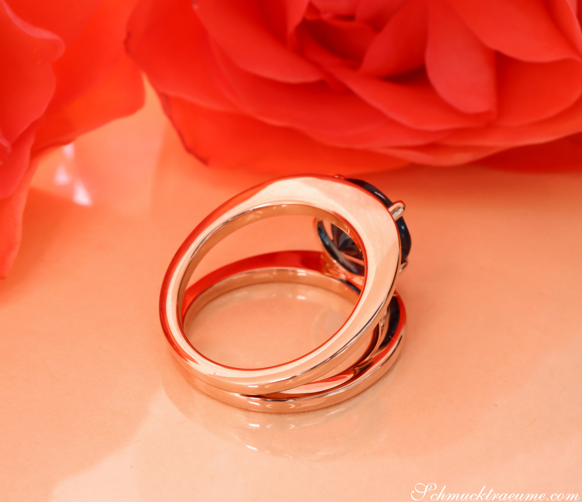 Runder Blautopas-Ring aus 585er Roségold mit klaren Linien auf rosafarbenem Hintergrund