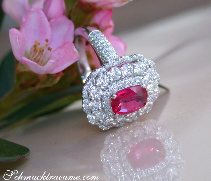 Weißgoldring mit ovalen Rubin und brillantenbesetzter Krone, Detailansicht, rosa Blume im Hintergrund.