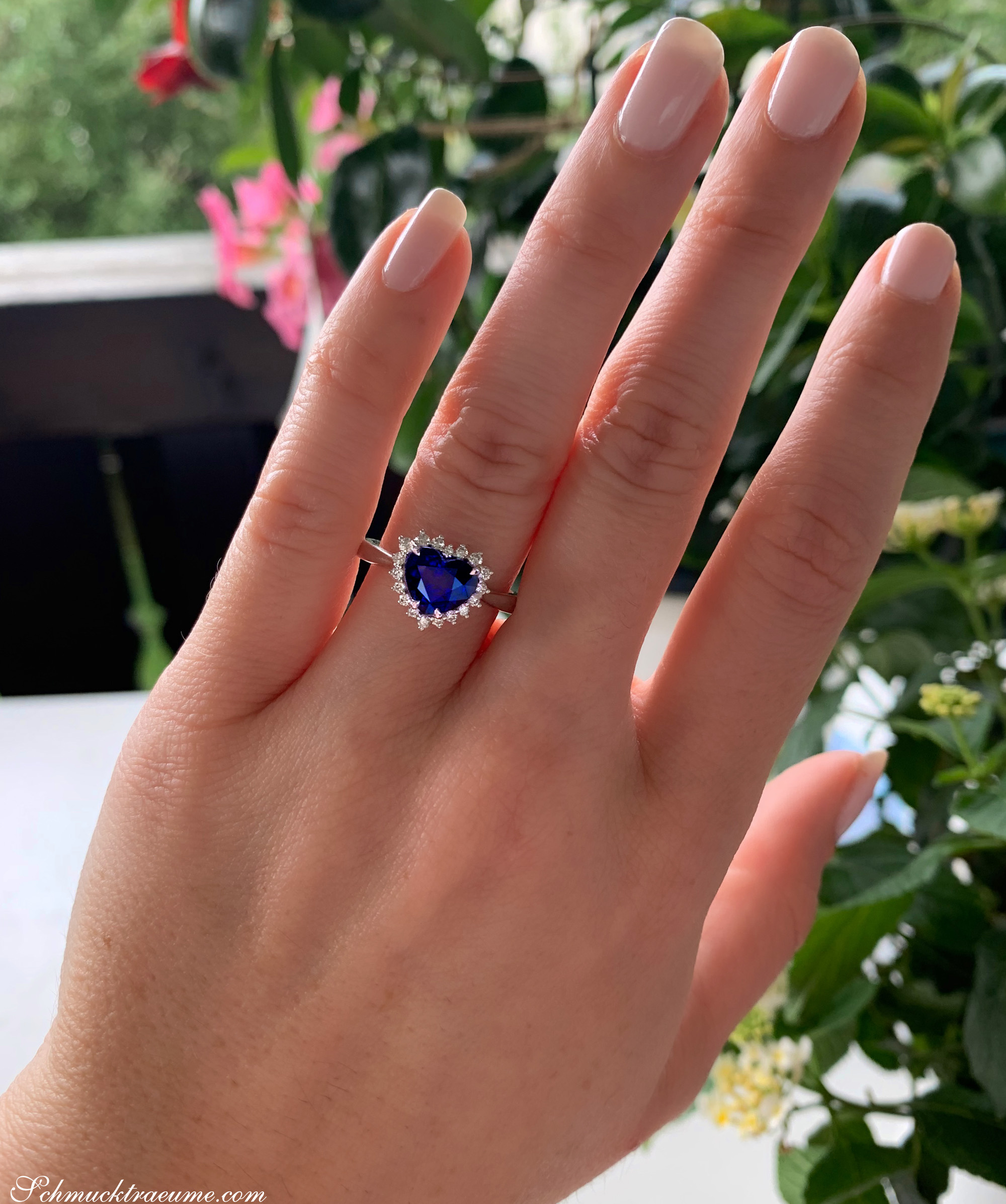 Klassischer Saphir Herz Ring mit Brillanten auf der Hand, umgeben von Pflanzen