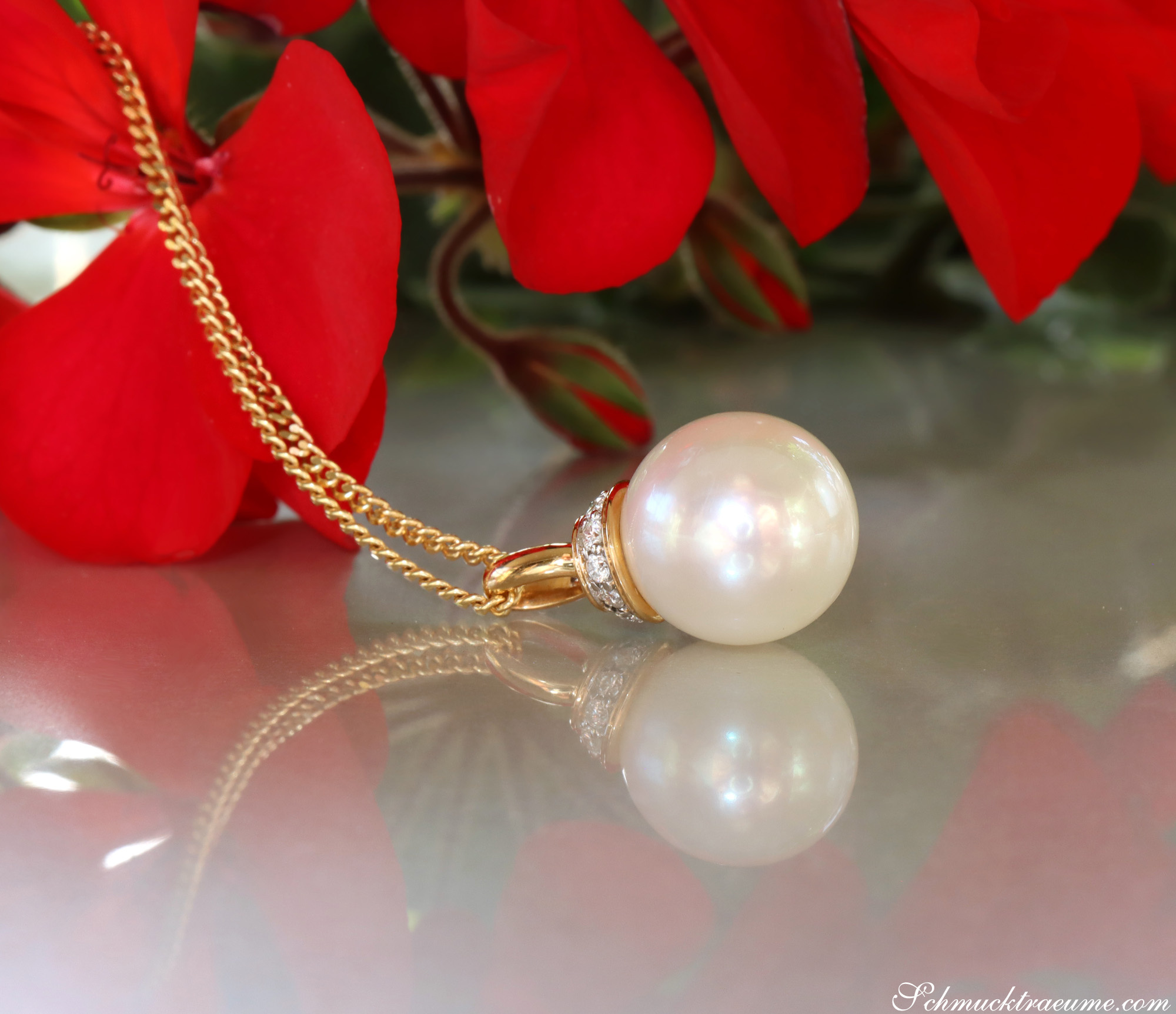 Goldkette mit Perlenanhänger und Brillanten vor roten Blüten