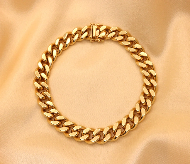 Goldene Panzerarmband mit Kurbelverschluss, Detailaufnahme auf cremefarbenem Stoff. Goldene Panzerarmband mit Kurbelverschluss, Detailaufnahme auf cremefarbenem Stoff.