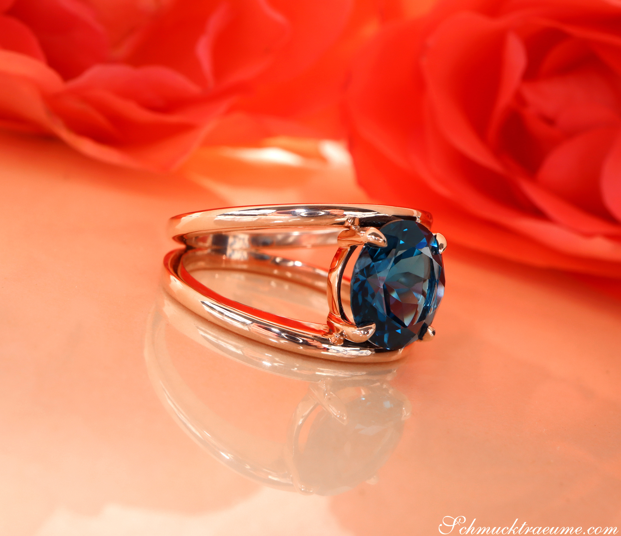 Blautopas-Ring in 585er Roségold, minimalistisch gestaltet, vor rotem Hintergrund