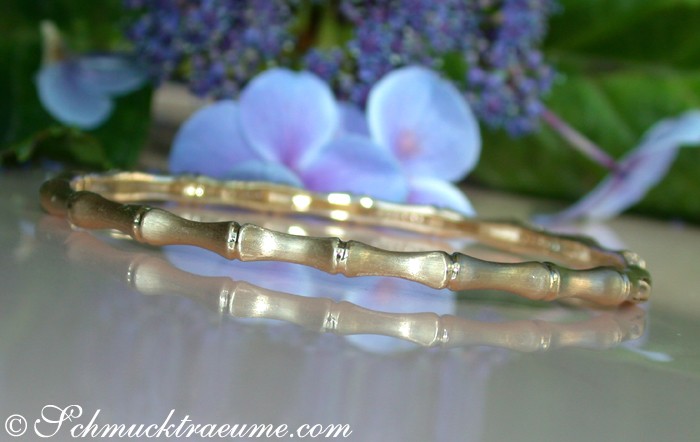Satiniertes Gelbgold Armband im Bambus-Design mit Diamanten, vor Blüten.