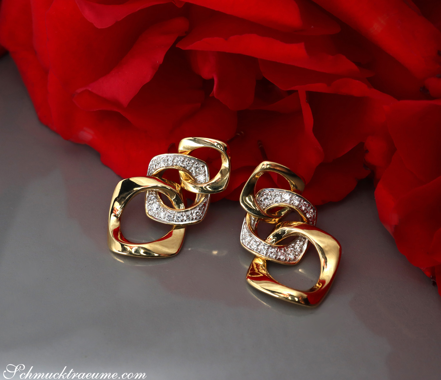 Goldene Ohrringe im Glieder-Design mit Brillanten, vor rotem Rosenblütenhintergrund.