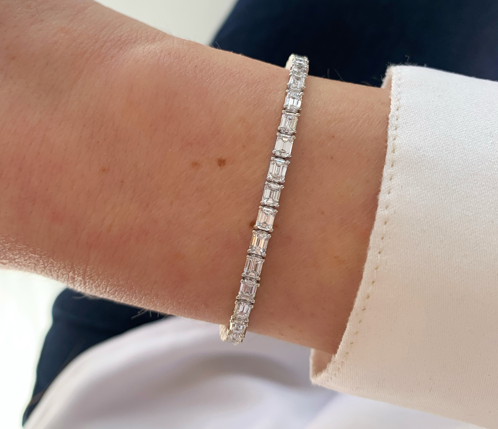 Diamant-Tennisarmband im Smaragdschliff auf Hand mit weißem Ärmel