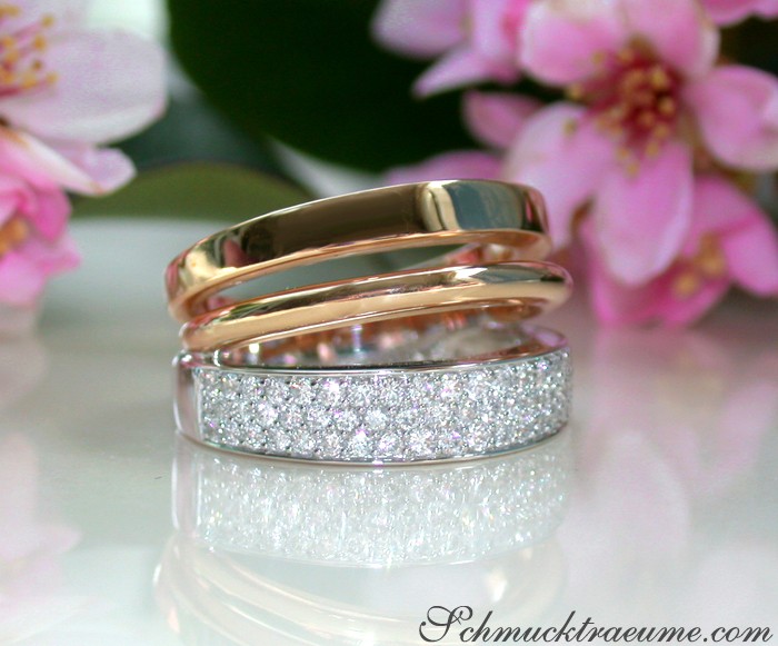 Goldene Mehrreihige Diamantringe auf glänzender Oberfläche, Hintergrund mit Blüten