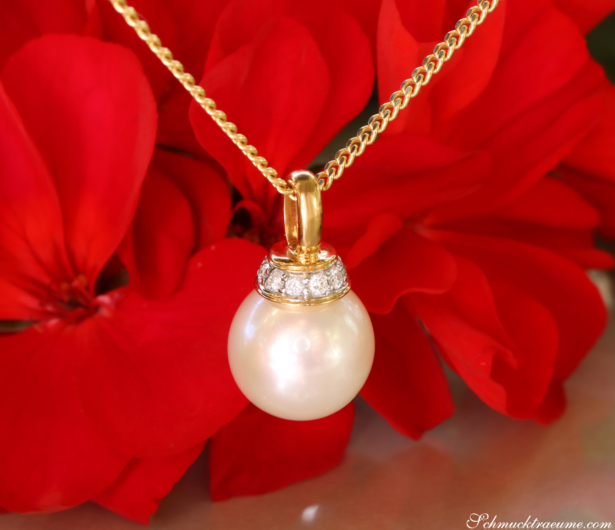 Goldkette mit Perlenanhänger und Brillanten vor roten Blütenblättern