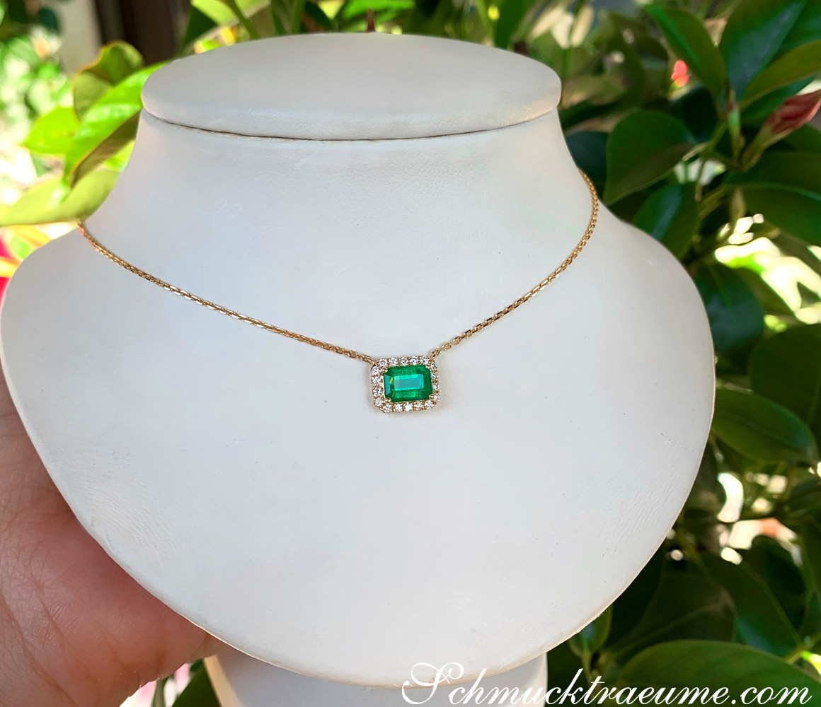 Smaragd-Halskette mit Brillanten in Gelbgold 585, präsentiert auf weißem Halsform-Modell, umgeben von grünen Blättern.