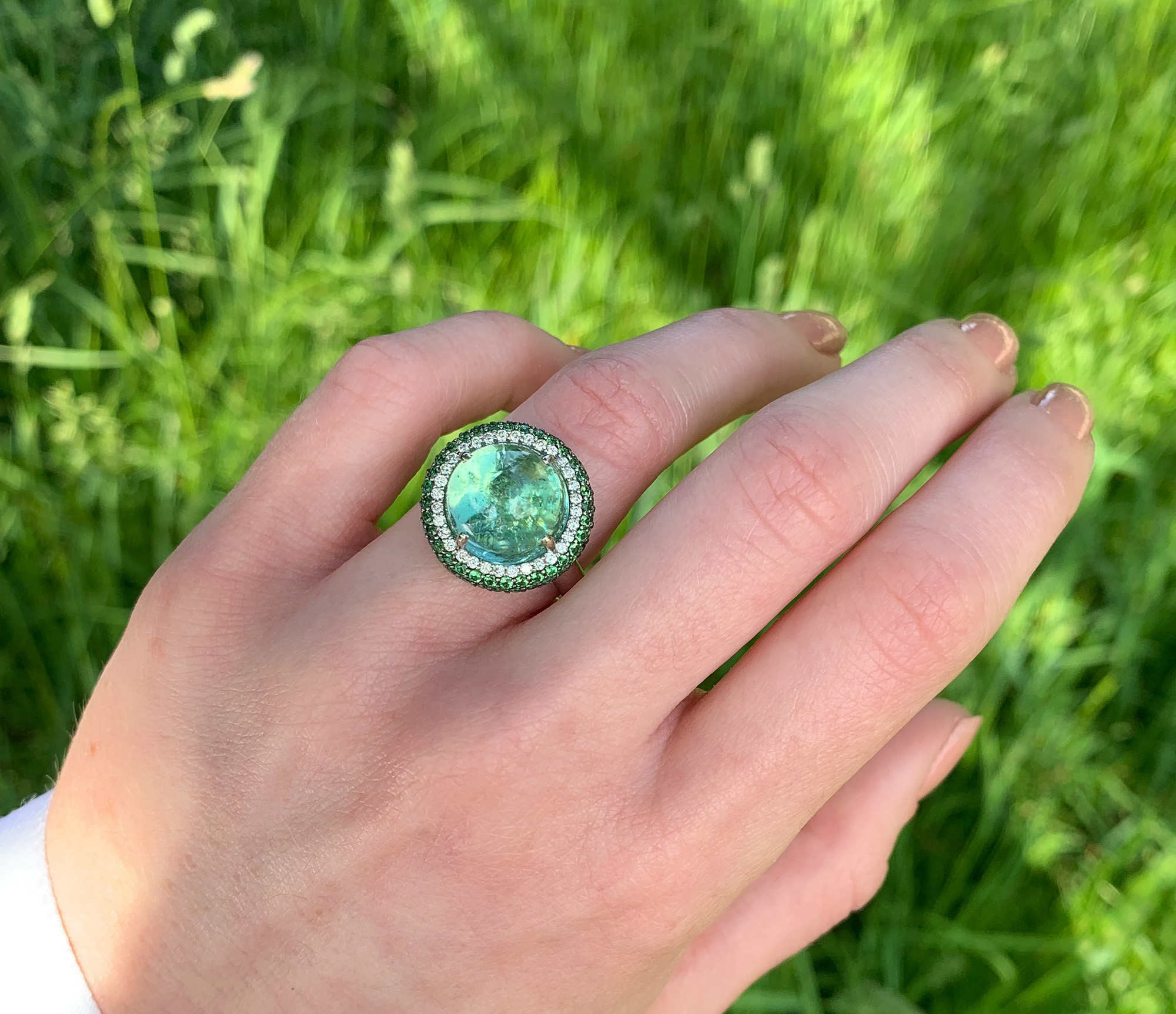 Mint-Turmalin-Ring mit Tsavorite und Brillanten auf Hand vor Gras.