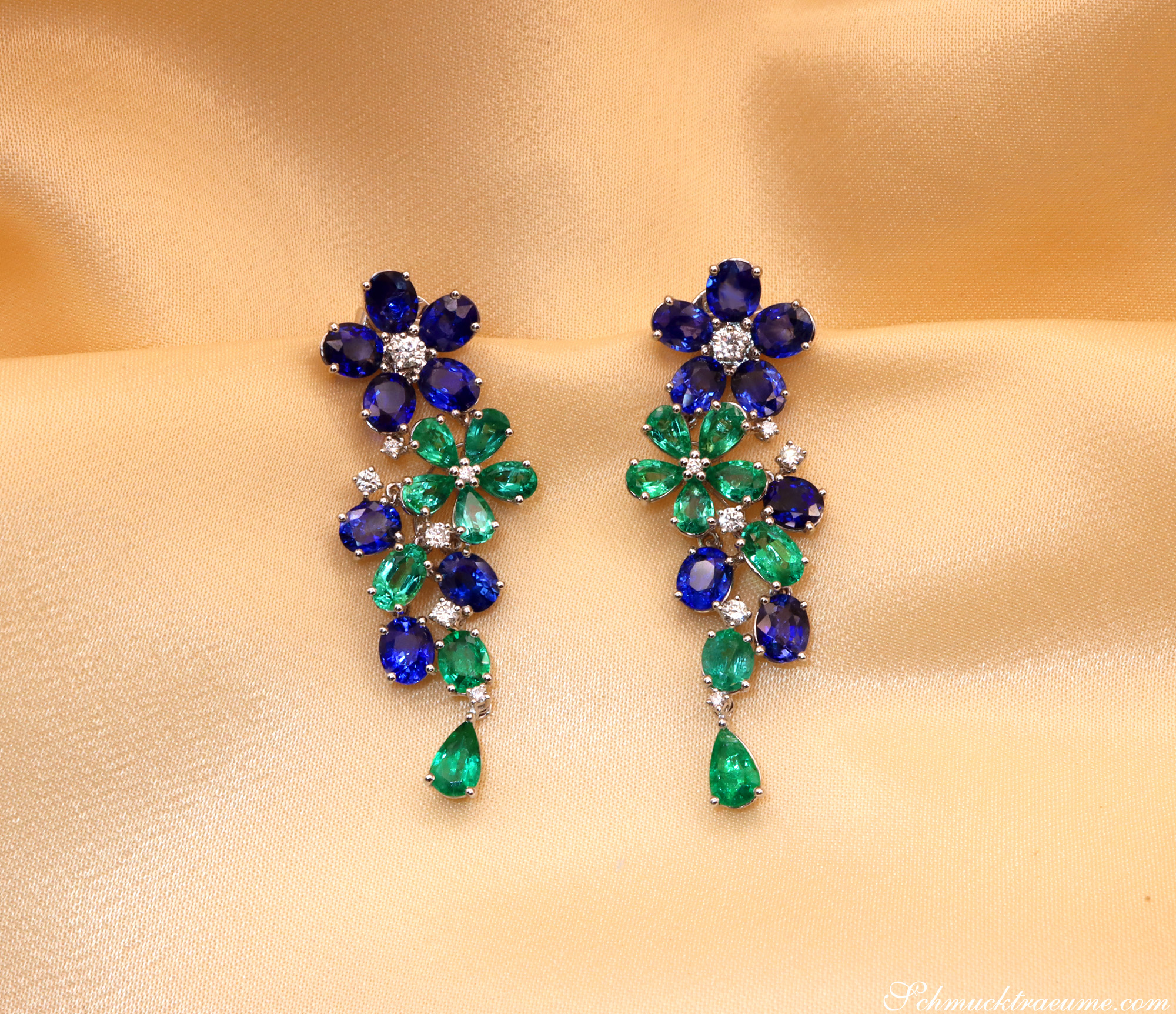 Blütenformige Ohrgehänge mit Smaragden und Saphiren auf Seidenhintergrund