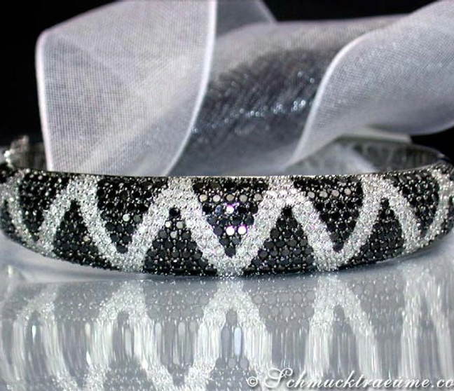 Silberner Zig-Zag-Armreif mit schwarz-weißen Diamanten auf weißem Tuch, Detailaufnahme Silberner Zig-Zag-Armreif mit schwarz-weißen Diamanten auf weißem Tuch, Detailaufnahme