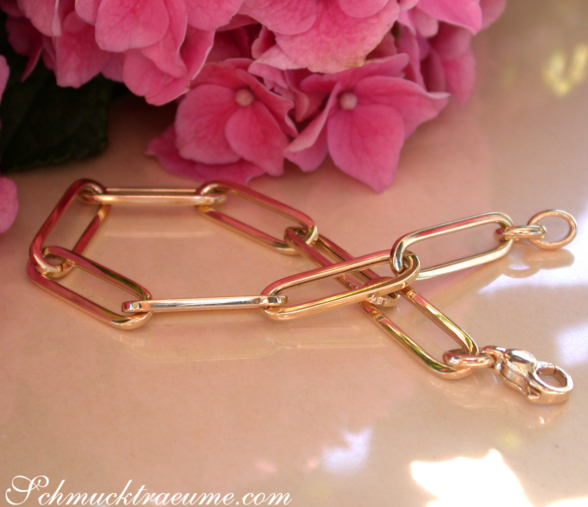 Goldenes Paperclip-Armband mit klaren Linien und lang gezogenen Gliedern vor rosa Hortensienblüten.