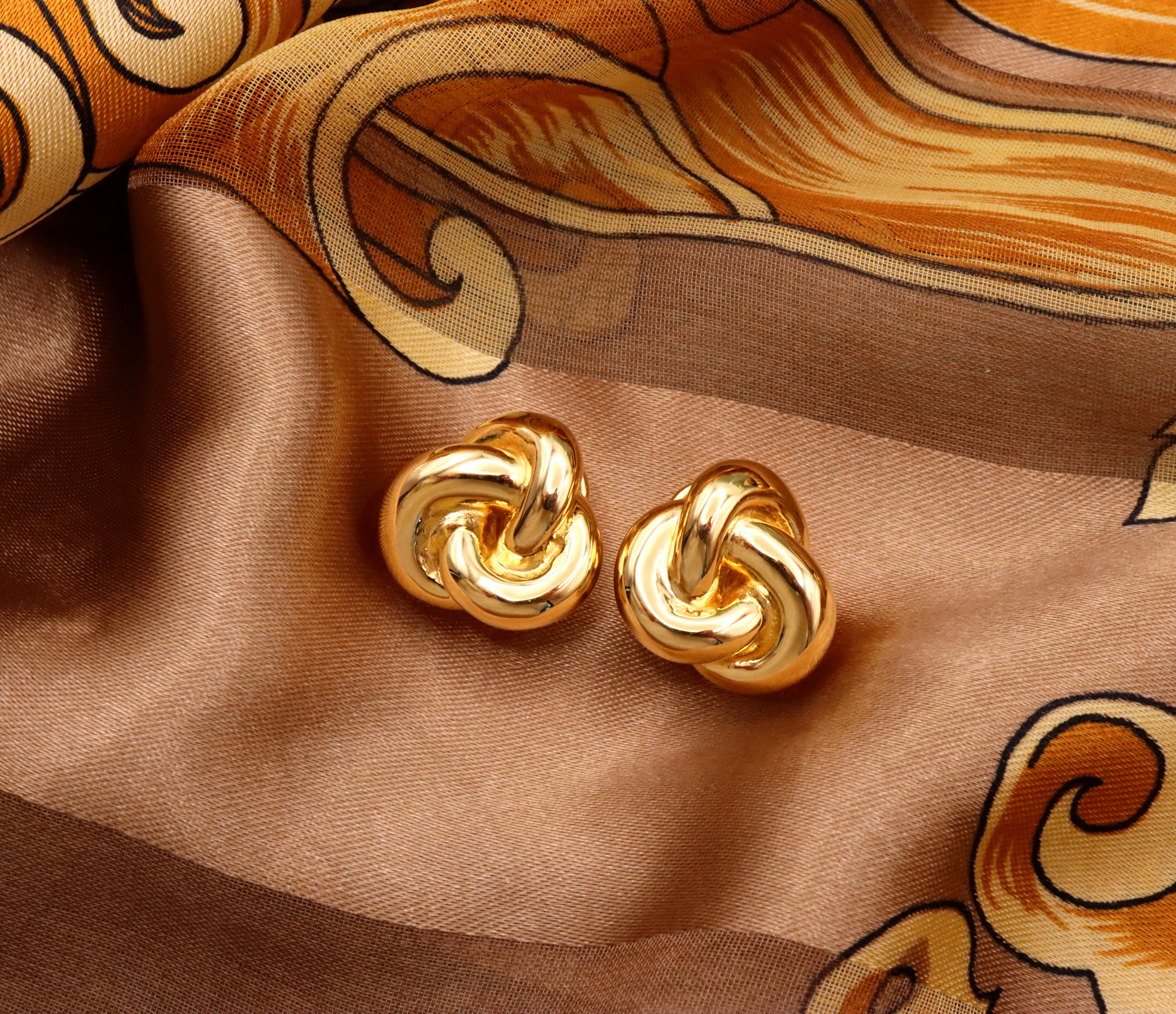 Goldene Knoten-Ohrstecker auf goldenem Stoff mit Ornamenten