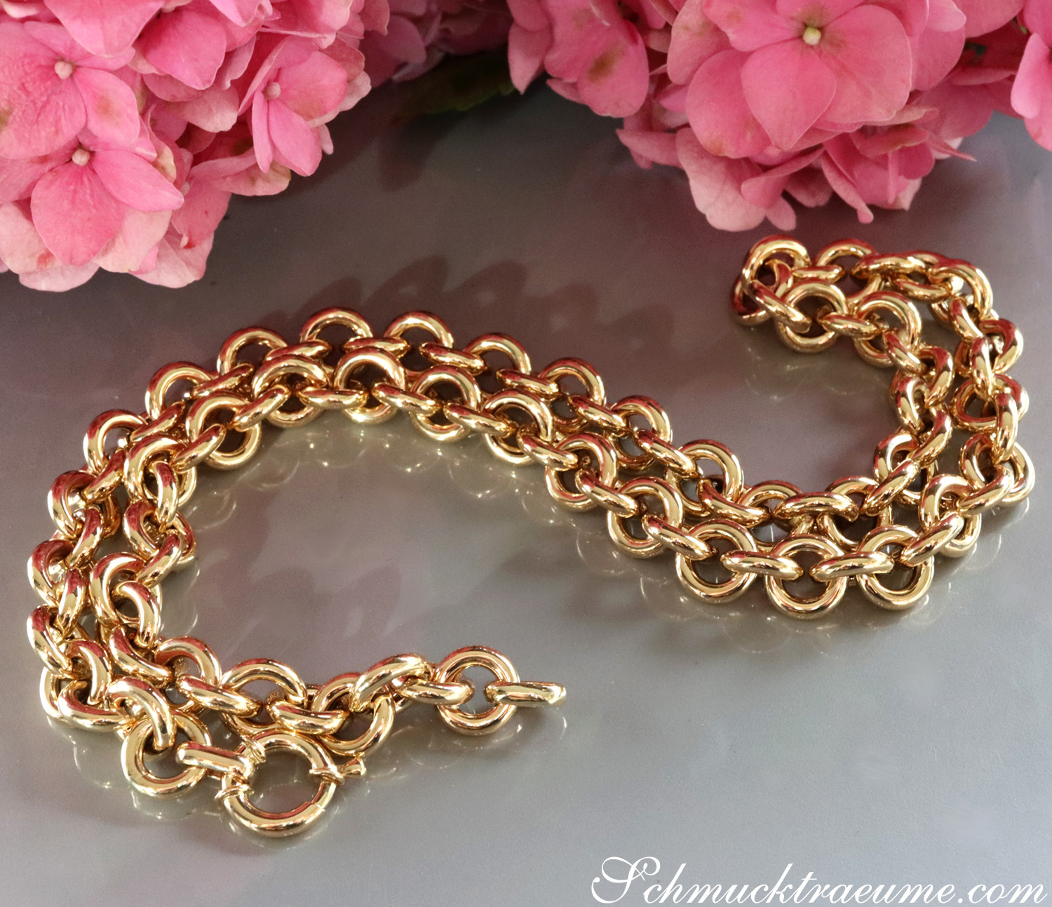 Goldene Gliederkette auf glattem Hintergrund, rosafarbene Blumen im Hintergrund.