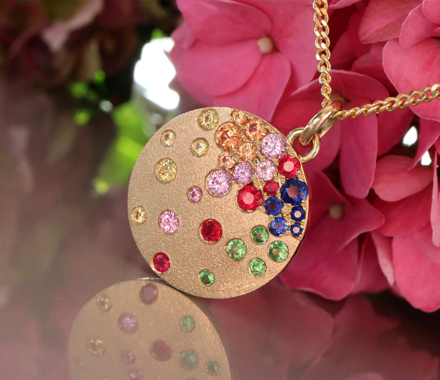 Goldene Medaillon-Halskette mit farbenfrohen Saphiren, Rubinen und Tsavorites, blühende Blüten im Hintergrund
