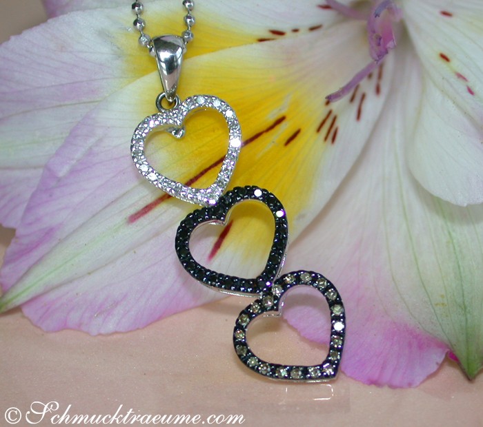 Weißgold Herzanhänger mit Diamanten, Detailaufnahme, drei Herzformen, Farbspiel, zarte Blume im Hintergrund