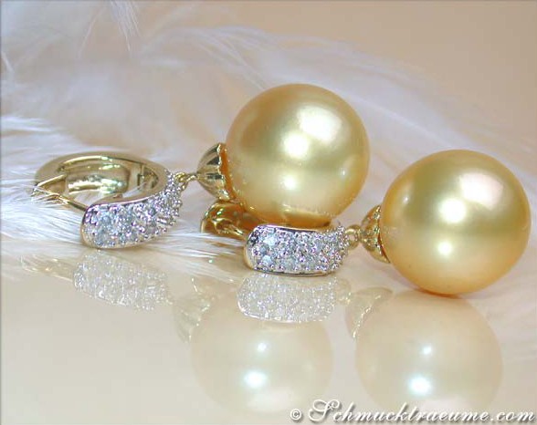 Goldene Südseeperlen-Ohrringe mit Diamanten, Detailansicht auf Federhintergrund.