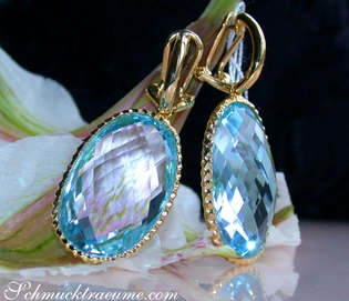 Goldene Ohrringe mit blauem Kristall, Detailaufnahme auf Blume, elegant.