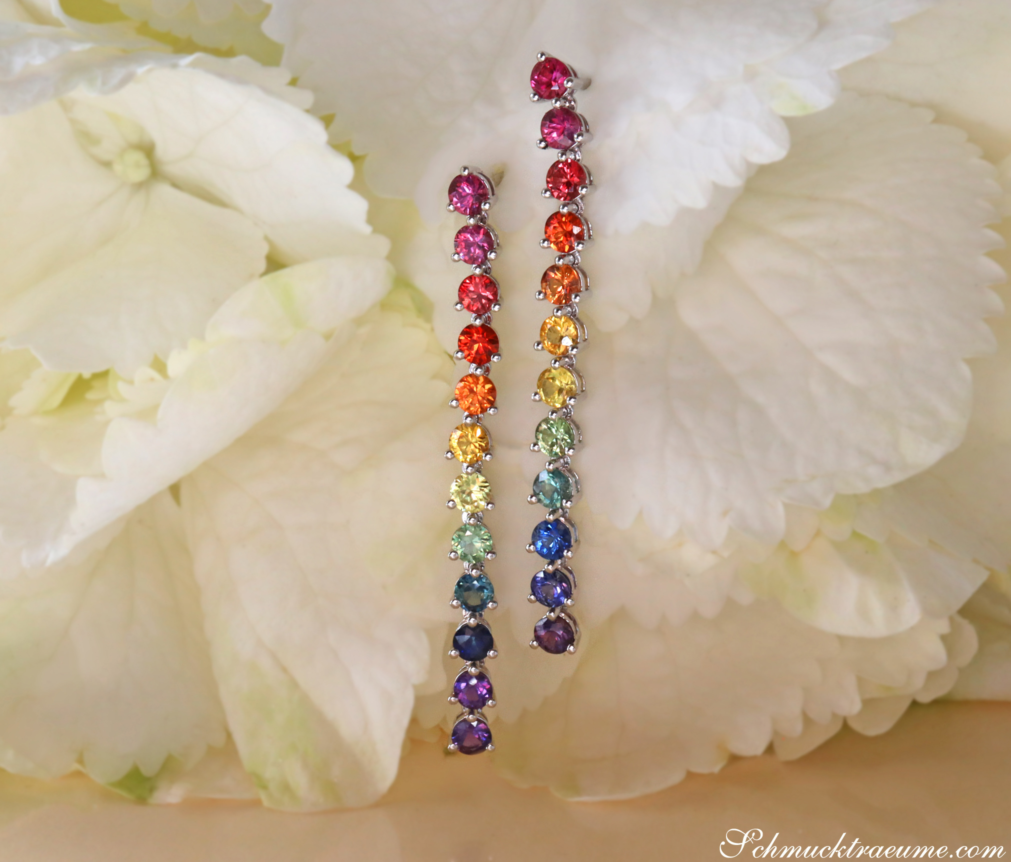 Weißgold-Ohrgehänge mit Regenbogen-Saphiren, Detailaufnahme auf Blütenhintergrund