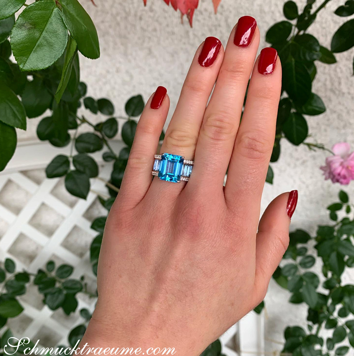 Blautopas-Ring mit Diamanten auf Hand vor Rosenblättern