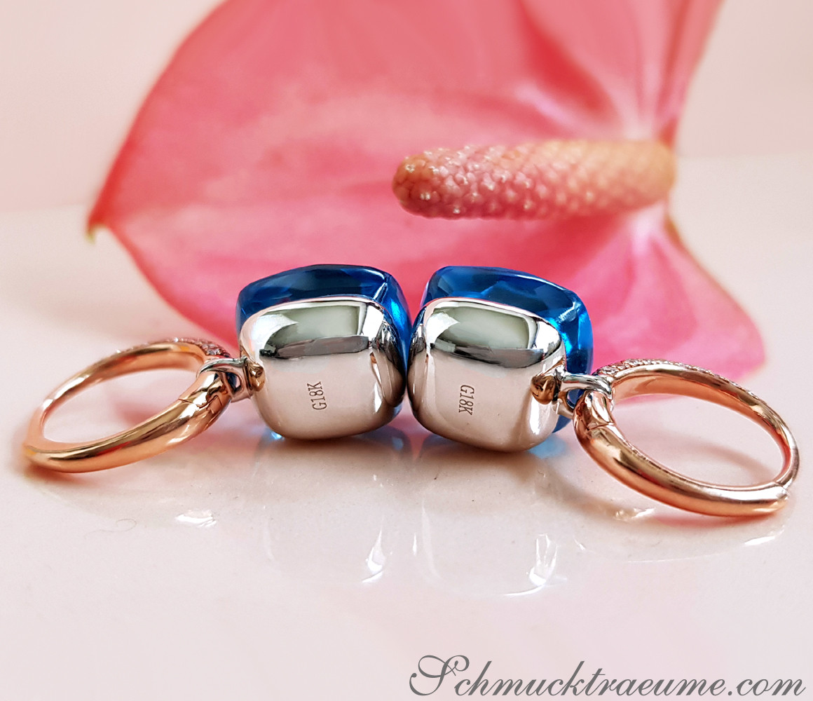 Blautopas-Ohrringe mit Diamanten, roségoldene Ringe, Blüte im Hintergrund
